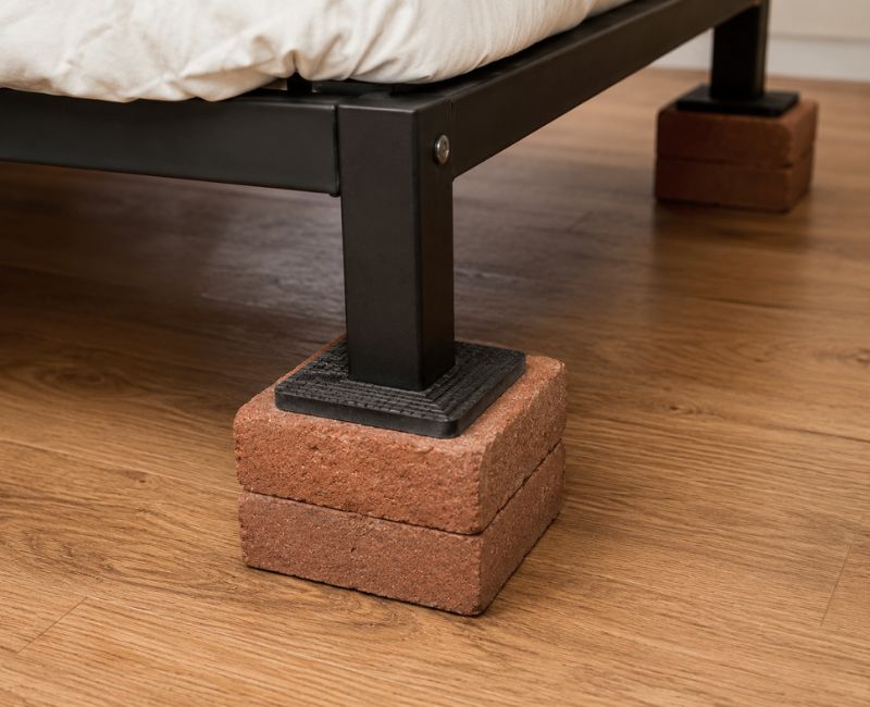 DIY brick bed risers with rubber padding protecting the floor and bed legs