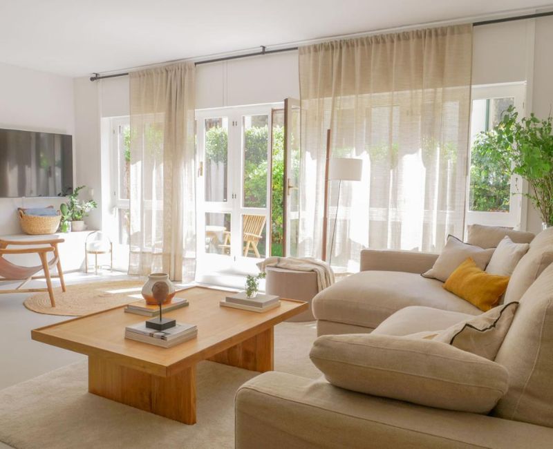 Modern living room with natural light, beige sofa, wooden coffee table, and indoor plants